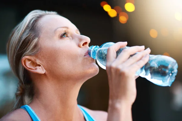 Nada sabe melhor do que a água depois de um treino intenso. Tiro de uma mulher madura bebendo água de uma garrafa ao ar livre. — Fotografia de Stock