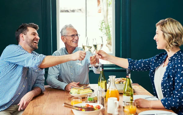 Makanannya luar biasa. Shot of a cheerful family sharing a celebratory toast together while being sitting around the dinner table at home. — Stok Foto