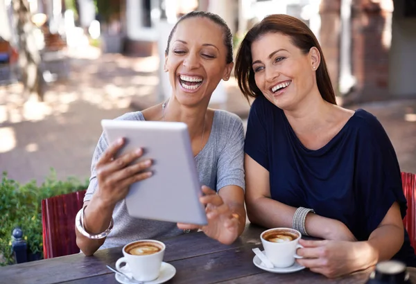 Laughing along with social media. Two young women looking at a tablet in a coffee shop. — Stock Photo, Image