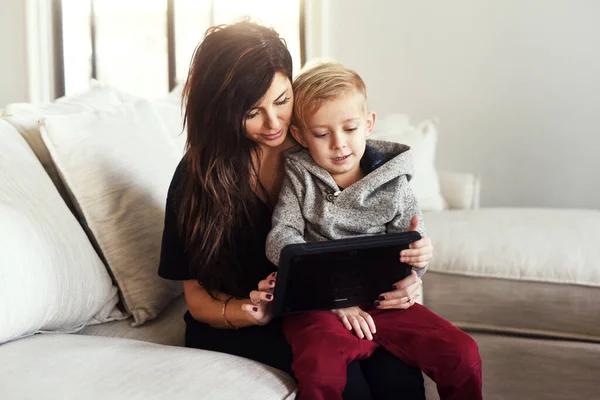 Lets see if we can find any cartoons. Shot of a carefree young woman browsing on a digital tablet with her little boy while being seated on a sofa at home during the day. — Photo