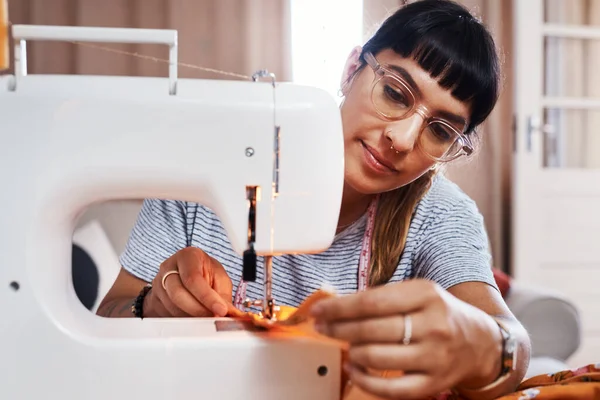 Ich liebe es einfach, Menschen in meinen wunderschönen Kreationen zu sehen. Schnappschuss einer jungen Frau, die zu Hause mit einer Nähmaschine Stoff näht. — Stockfoto