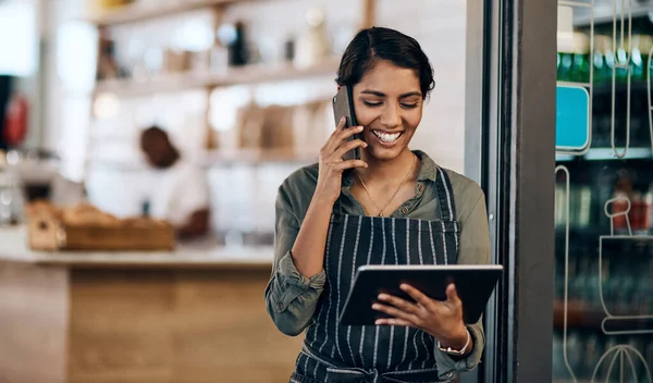 Le barista sans fil. Prise de vue d'une jeune femme utilisant une tablette numérique et un smartphone alors qu'elle travaillait dans un café. — Photo