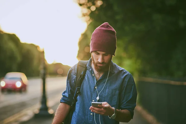 Οι βόλτες του περιλαμβάνουν πάντα μουσική. Μια φωτογραφία ενός όμορφου νεαρού που ακούει μουσική στο κινητό του ενώ περπατάει στην πόλη.. — Φωτογραφία Αρχείου