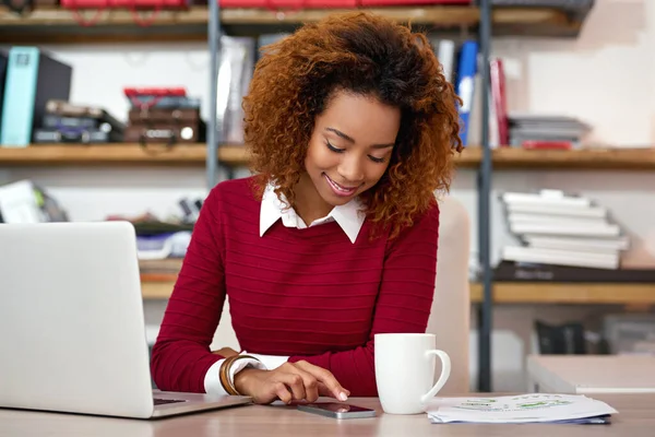 Checking her schedule for today. Shot of a young woman sending at text while working on a laptop in an office. — Foto de Stock