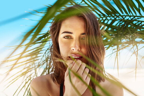 Oh what a beautiful summer. Shot of an attractive young woman standing under the shade of a palm tree at the beach. — Stock Photo, Image
