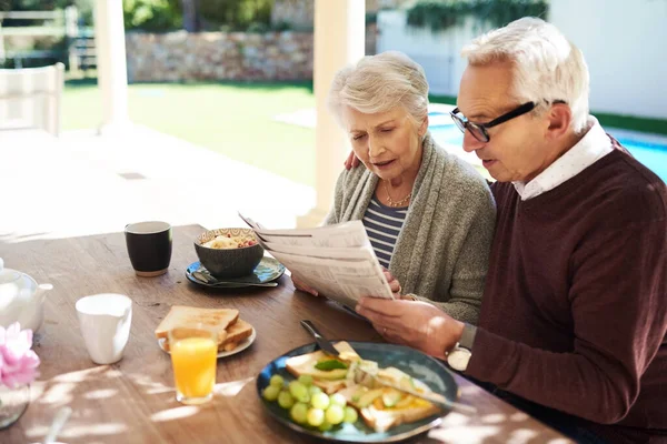 Те, що відбувається сьогодні зі світом. Знімок лагідної старшої пари, яка читає газету, насолоджуючись їжею разом на відкритому повітрі . — стокове фото