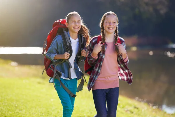 In un'avventura tra ragazze. Girato di due giovani ragazze che indossano zaini che camminano insieme accanto a un lago. — Foto Stock