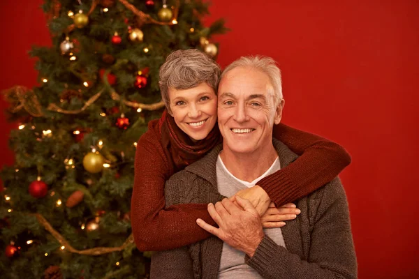 De här ska med på julkortet. Ett beskärt porträtt av ett lyckligt moget par framför en julgran. — Stockfoto