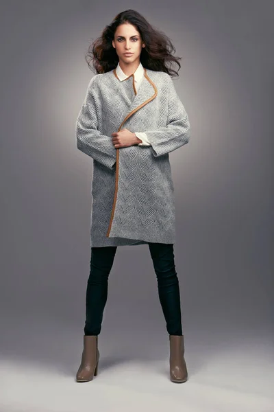 Kış modasıyla göz kamaştırıcı. Gri bir arka planda şık giyinmiş genç bir kadının stüdyo fotoğrafı.. — Stok fotoğraf