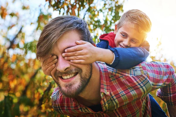 Can you see. Cropped shot of an adorable young boy closing his fathers eyes while being piggybacked outside during autumn. — Foto de Stock