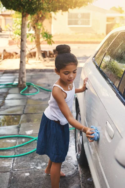 Shes so young but helpful. Shot of a young girl busy cleaning a car outside. — Foto de Stock