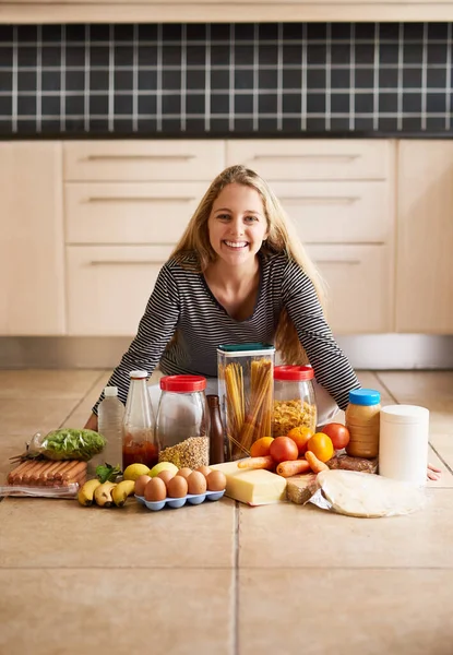 Everything I need for a yummy meal. Shot of an attractive young woman surrounded by various food in the kitchen at home. — Foto de Stock