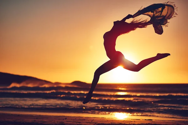 The best freedom is being yourself. Silhouette of an energetic woman jumping on the beach at sunset. — Foto de Stock