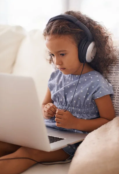 Ontwikkeling van de jeugd in het digitale tijdperk. Shot van een klein meisje met behulp van een koptelefoon en een laptop terwijl thuis zitten. — Stockfoto