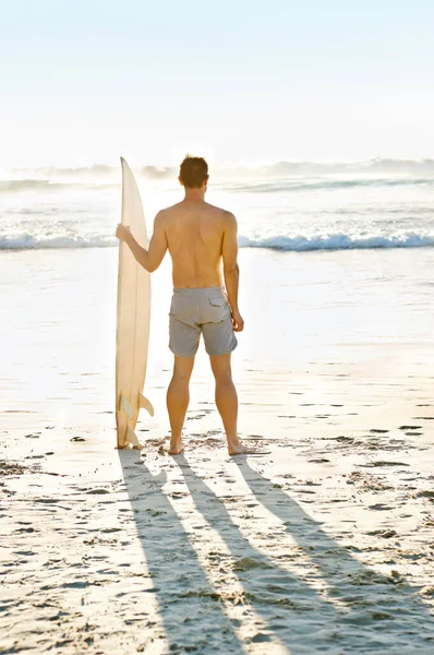 Ive never seen a more beautiful view. Rearview shot of a muscular young man holdng his surfboard while on the beach. — ストック写真