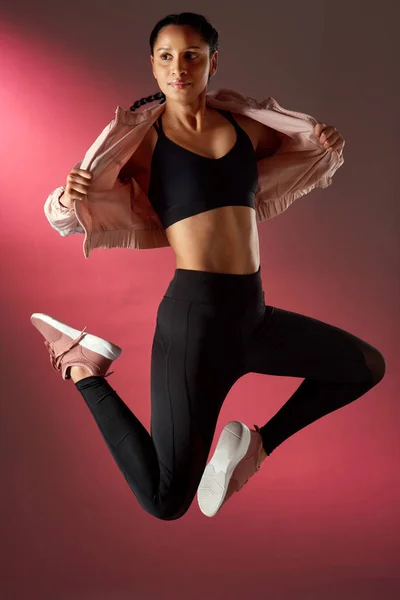 Το σώμα της είναι τόσο καλά τονισμένο. Στιγμιότυπο στούντιο μιας αθλητικής νεαρής γυναίκας που πηδάει πάνω σε κόκκινο φόντο. — Φωτογραφία Αρχείου
