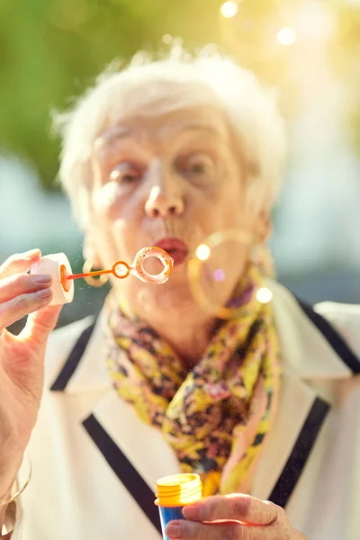 Ő egy arany öreglány. Egy vidám idős nőről, aki buborékokat fúj odakint egy napsütéses napon.. — Stock Fotó