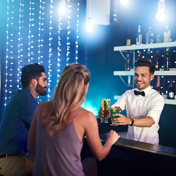 Su habilidad y personalidad mantienen satisfechos a sus clientes. Foto de un camarero feliz sirviendo bebidas a una pareja en un club nocturno. — Foto de Stock