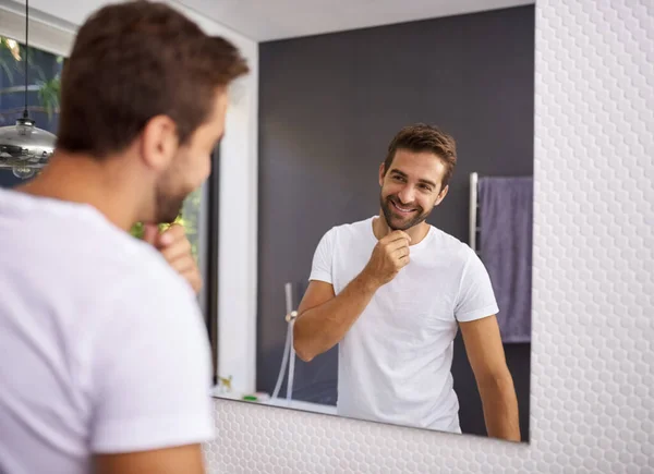 I do look good with a beard though. Cropped shot of a handsome man looking at himself in the mirror whilst touching his beard at home. — стоковое фото