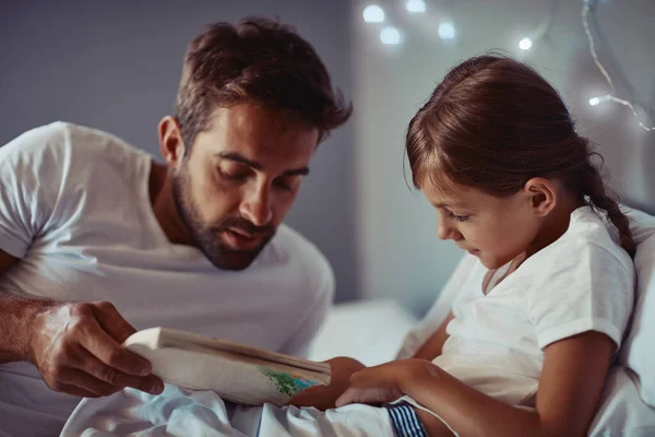 Je to nejklidnější a nejklidnější část dne. Vystřižený záběr otce, jak čte pohádku před spaním své holčičce. — Stock fotografie