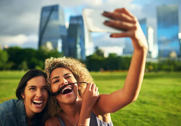 Nos encanta capturar nuestros momentos tontos. Recortado disparo de dos atractivas novias jóvenes posando para un selfie juntos en un parque. — Foto de Stock