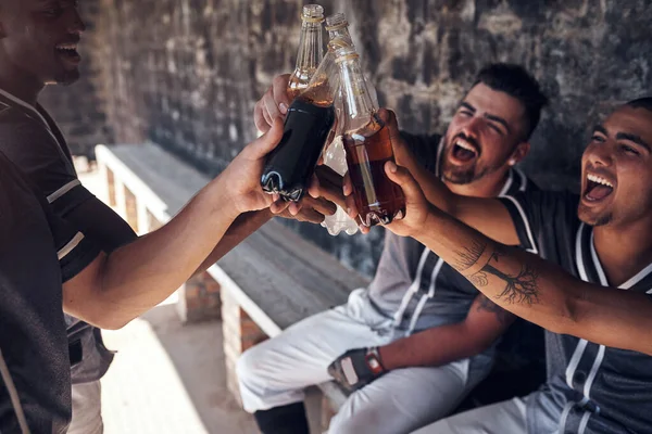 Come for the game, stay for the fun. Shot of a group of young men celebrating with drinks after playing a baseball game.