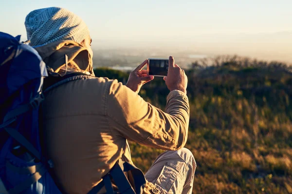 Every angle of nature is the perfect shot. Shot of a hiker on top of a mountain taking photos with his cellphone. — Foto de Stock