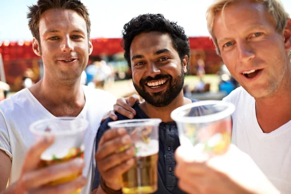 Ölkompisar som förenas. Tre unga män skålar sina öl på en musikfestival. — Stockfoto