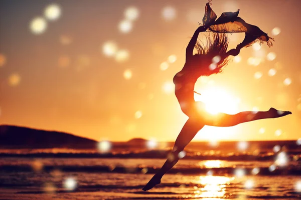 Nech tam, kam půjdeš, jiskru. Silueta energické ženy skákající po pláži při západu slunce. — Stock fotografie