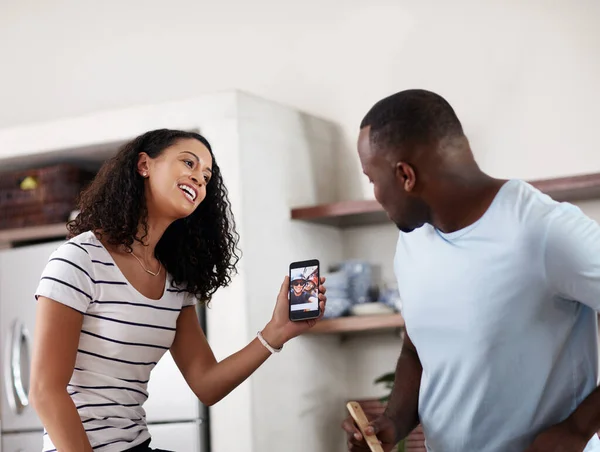 Verificar os perfis online dos nossos amigos. Tiro cortado de um jovem casal olhando para um celular juntos na cozinha em casa. — Fotografia de Stock