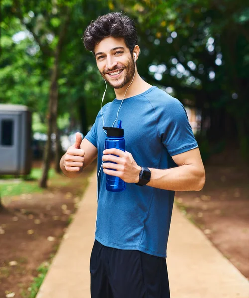 Youre well on your way to a better lifestyle. Portrait of a sporty young man holding a water bottle and showing thumbs up while exercising outdoors. — Foto de Stock