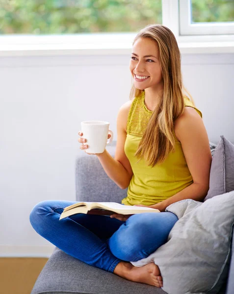 Káva a volný čas. Snímek mladé ženy, jak čte knihu na pohovce doma. — Stock fotografie