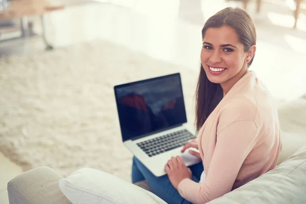Зв'язок у будь-якому місці будинку. Портрет усміхненої молодої жінки, яка використовує ноутбук, розслабляючись на дивані вдома . — стокове фото