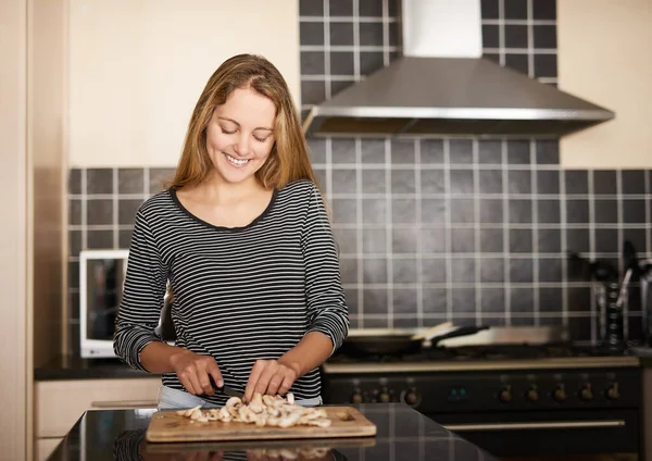 Mushrooms are the secret ingredient. Shot of a happy young woman slicing mushrooms on a chopping board in the kitchen. — Foto de Stock