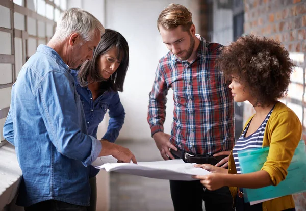 Pointing out the genius in his plans. A group of colleagues standing in a building and assessing blueprints. — Photo