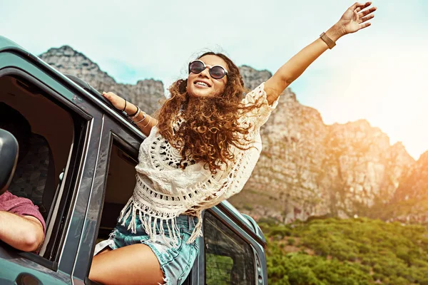 Bring on the good times. Cropped shot of a young woman leaning out a car with her arms outstretched while on a roadtrip. — Stock Photo, Image