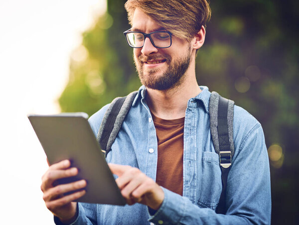 Stay connected even in nature. Cropped shot of a handsome young man using a tablet outdoors.