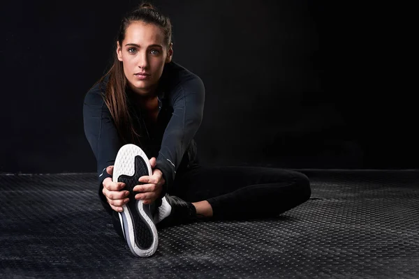 Mantenerse flexible y fuerte. Retrato de estudio de una joven vestida con ropa de gimnasia estirando sus piernas sobre un fondo oscuro. —  Fotos de Stock
