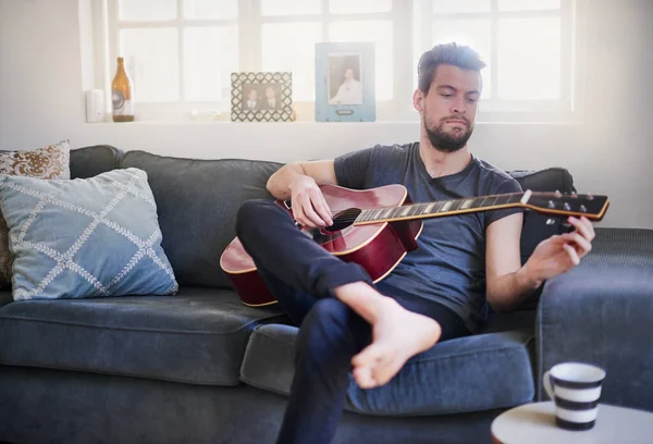 Ele desenvolveu um ouvido musical bem afinado. Tiro cortado de um jovem bonito tocando guitarra em casa. — Fotografia de Stock