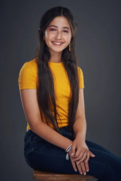 When all else fails, smile. Cropped portrait of an attractive teenage girl sitting alone against a dark background in the studio. — Photo