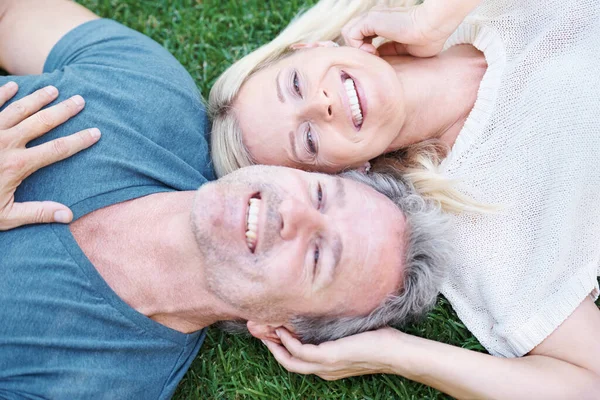 Ευχάριστη χαλάρωση φέρνει την ευτυχία. Ένα ώριμο ζευγάρι ξαπλωμένο στο γρασίδι και κοιτάζοντάς σε χαρούμενο. — Φωτογραφία Αρχείου