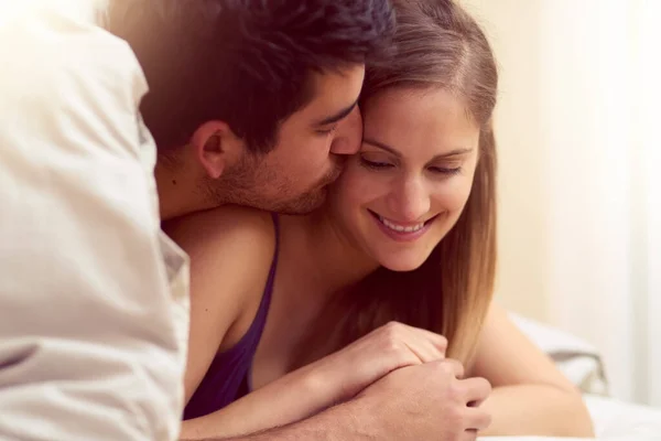 Jeder Kuss fühlt sich wie der erste an. Aufnahme eines liebenden jungen Paares, das sich einen Kuss teilt, während es zusammen unter einer Decke liegt. — Stockfoto
