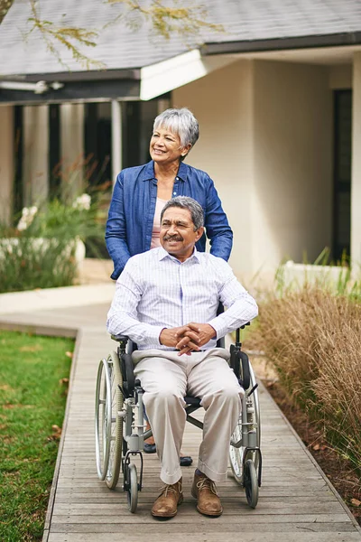 Out for a stroll. Shot of a senior woman pushing her husband in a wheelchair outside. — Stock Photo, Image
