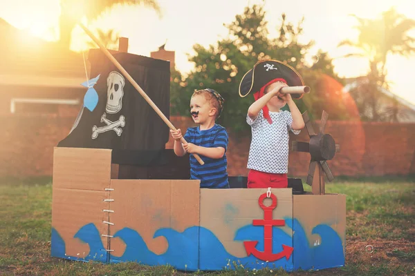 Questi piccoli pirati vogliono solo divertirsi. Girato di un bambino carino e suo fratello che giocano ai pirati fuori su una barca fatta di scatole di cartone. — Foto Stock