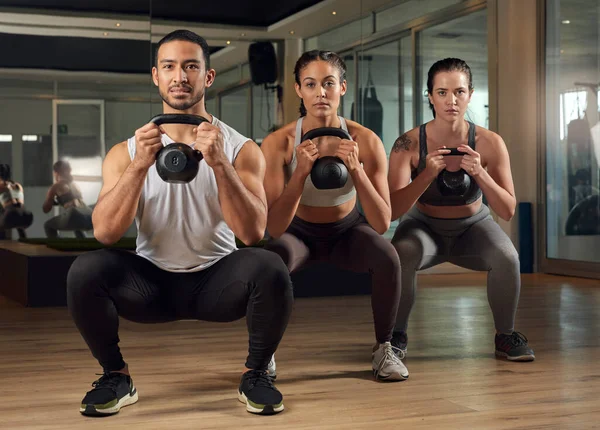 Dzwony czajnikowe to świetny trening. Portret trójki młodych sportowców ćwiczących z dzwonkami na siłowni. — Zdjęcie stockowe