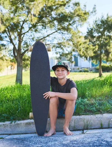 Learning how to skate. Full length portrait of a young boy sitting on the curb with his longboard. — Stock Photo, Image