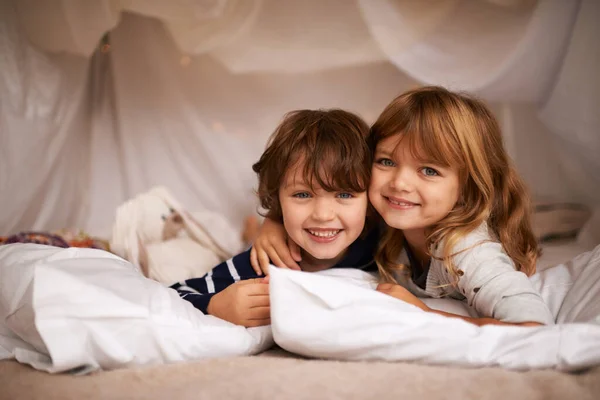 Geschwister machen die besten Freunde. Aufnahme von zwei entzückenden Geschwistern, die in ihrem Deckenfort im Haus liegen. — Stockfoto