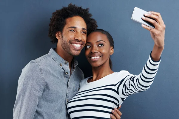 Ny profilbild. Skjuten av ett lyckligt ungt par tar ett foto av sig själva med en mobiltelefon på en grå bakgrund. — Stockfoto