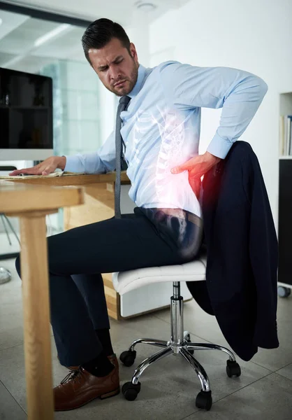 Work demands are taking a toll on his health. Shot of a young businessman experiencing back pain highlighted in glowing red at work. — Stock Photo, Image