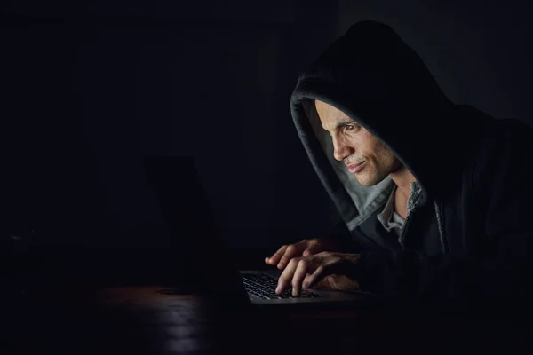 Protect yourself before its too late. Shot of a hooded computer hacker using a laptop in the dark. — Foto de Stock